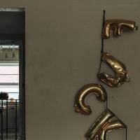 Person collapsed at kitchen table seen through door way. Deflated letter balloons spell out "F U C K"